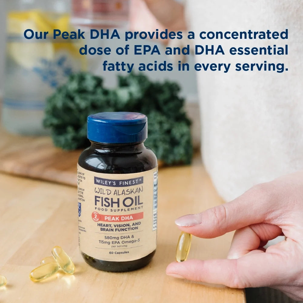 Person holding Wiley’s Finest PEAK DHA bottle beside omega-3 capsules