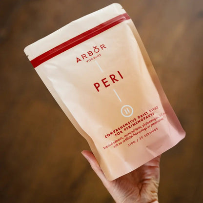 Hand holding an Arbor Vitamins PERI Blend powder pouch in a lifestyle setting