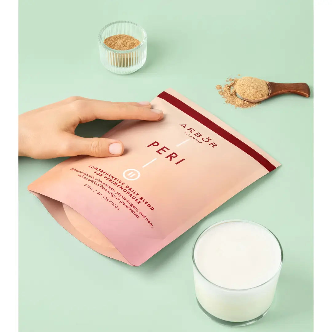 Hand holding an Arbor Vitamins PERI Blend pouch beside a prepared drink and spoonful of powder